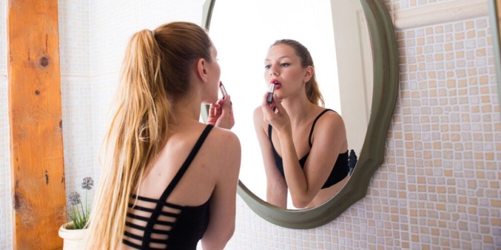 Woman in black sports bra doing her makeup in the mirror