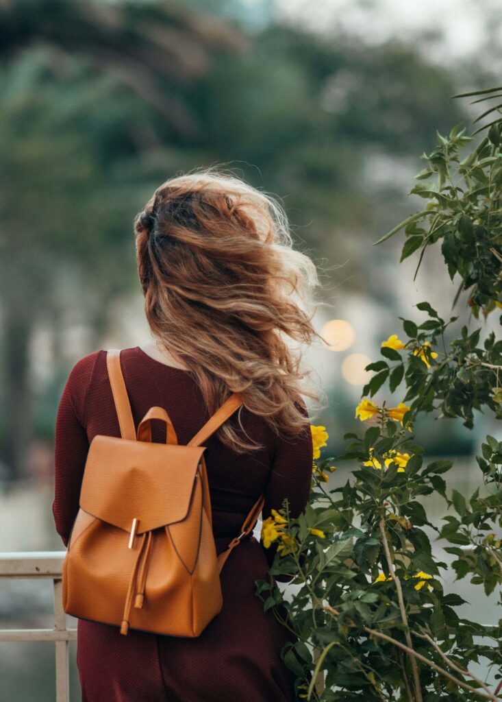 girl with an orange leather backpack by a yellow flower bush